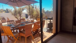 Un espace de restauration en plein air avec des tables et des chaises en bois, un grand parasol et une vue sur le jardin.