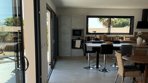 Une cuisine moderne avec un coin repas, de grandes fenêtres et une vue sur l’extérieur.