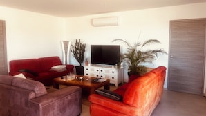 Un salon avec un canapé rouge, un fauteuil en cuir marron, une table basse en bois, un téléviseur à écran plat et une plante en pot.