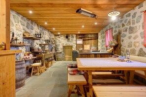 Un intérieur rustique avec des murs en pierre, des poutres en bois, un sol en pierre et une table en bois accompagnée de bancs.