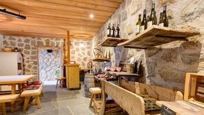 A rustic cellar with wooden benches, stone walls, and wine bottles on shelves.