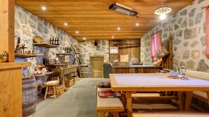 A rustic interior with stone walls, wooden beams, a stone floor, and a wooden table with benches.