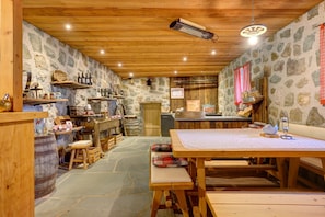 A rustic interior with stone walls, wooden beams, a stone floor, and a wooden table with benches.
