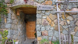 A stone building entrance with a wooden door, a sign reading 'Hofladen,' and a wooden fence.