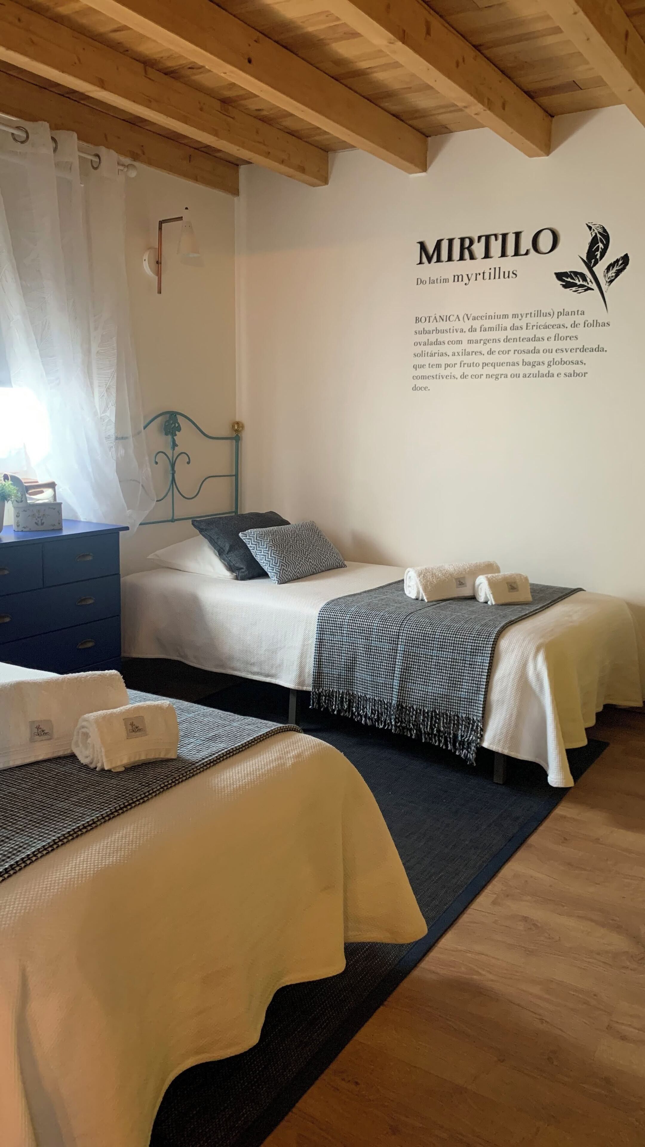 A cozy bedroom with two beds, a wooden ceiling, and a wall-mounted sign.
