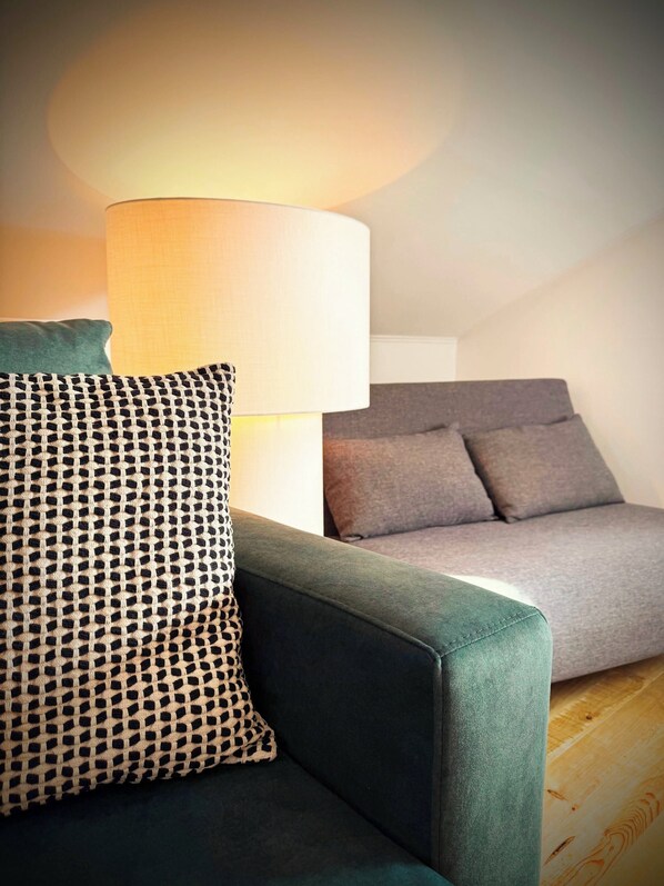 A modern living room with a green sofa, a patterned throw pillow, and a grey couch.