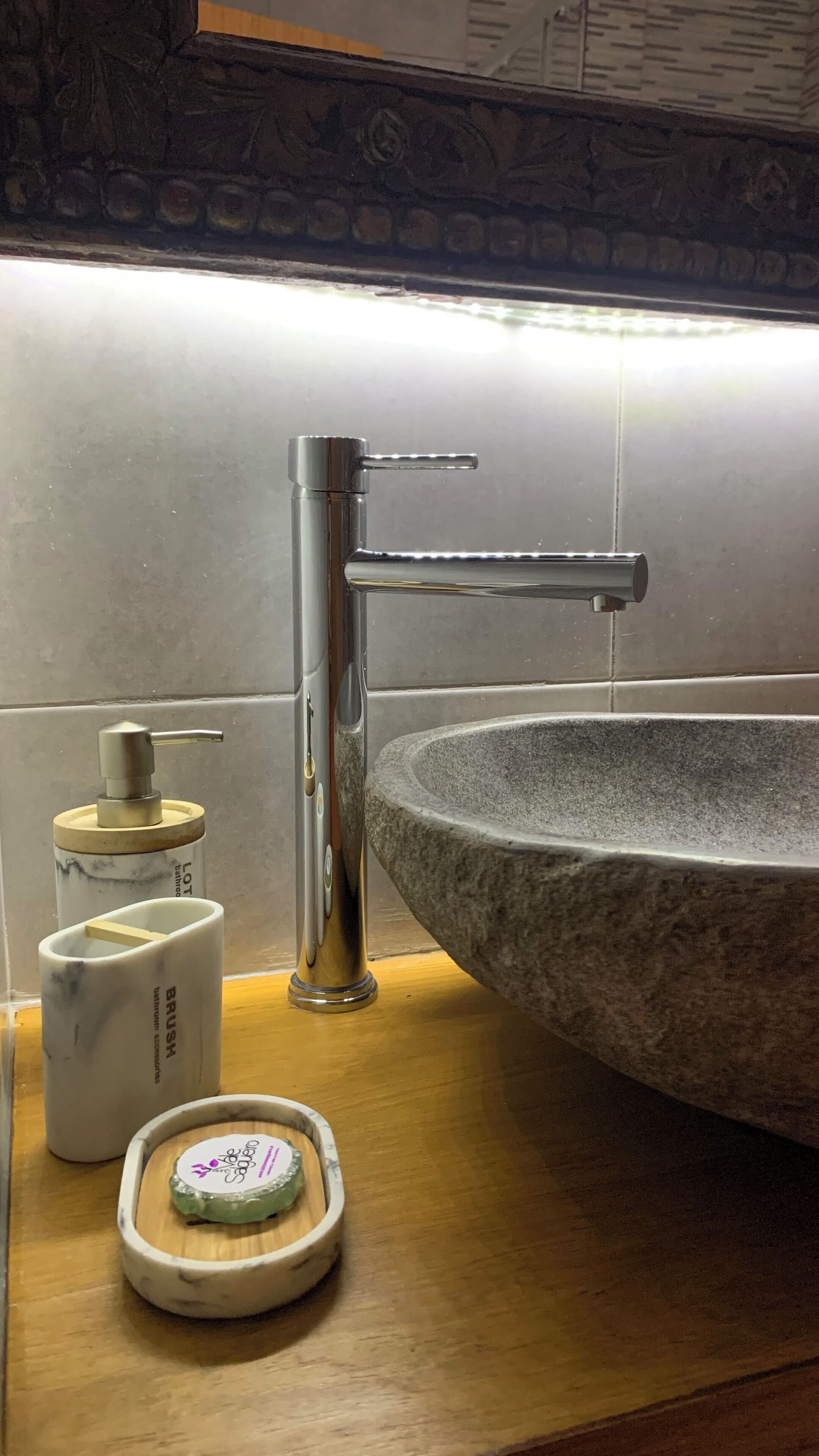 A bathroom with a stone sink, a modern faucet, and a soap dispenser on a wooden countertop.