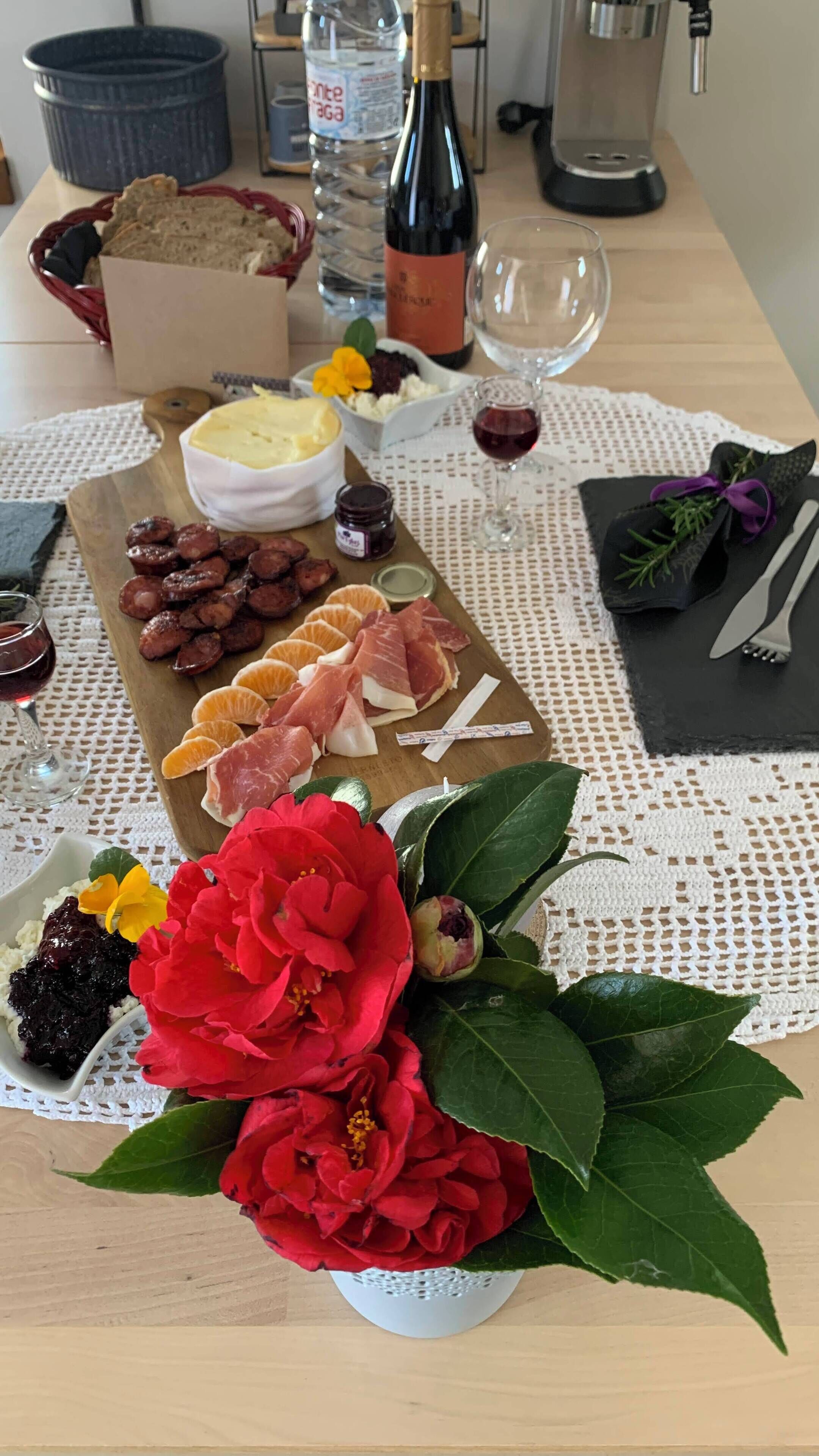 A charcuterie board with various meats, cheeses, and fruits, accompanied by a bottle of wine and a glass of red wine.