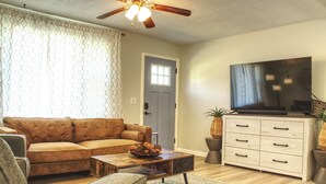 A living room with a brown leather sofa, a wooden coffee table, a TV on a stand, and a large painting on the wall.