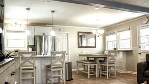 A modern kitchen with white cabinetry, a dining area with a wooden table and chairs, and a large mirror above the table.