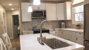 A kitchen with white cabinets, a stainless steel sink, a microwave, and a coffee maker.