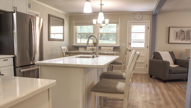A modern kitchen with a central island, stainless steel appliances, and a dining area with a gray sofa.