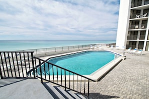 A swimming pool with a view of the ocean, lounge chairs, and a building with balconies. - 🏖️Gulf Front-Hot Tub-Pool-Aquavista 603W🏖️ (Panama City Beach)