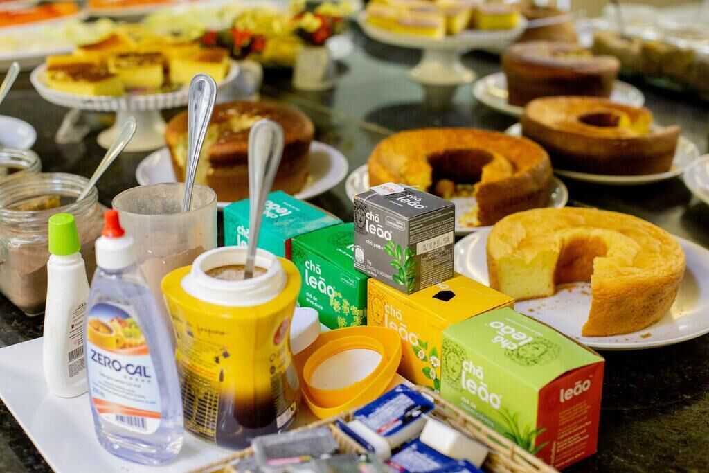 A table with various food items and condiments, including cakes and boxes of 'Chá Leão' tea.