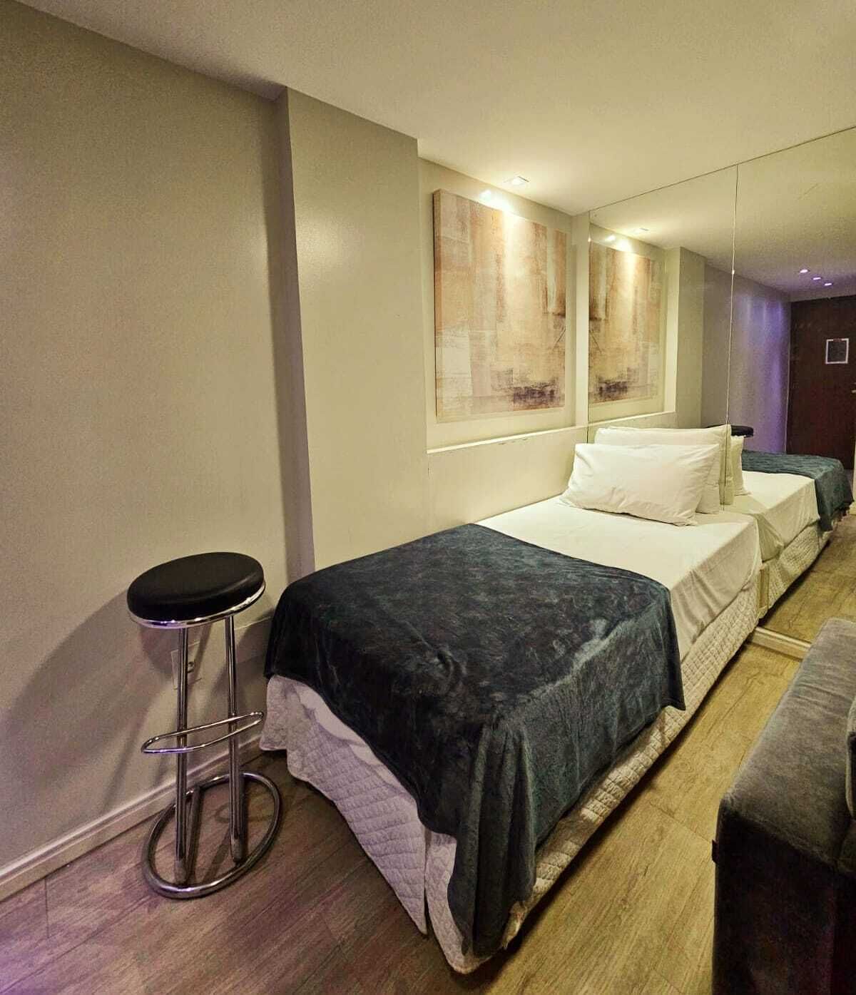 Quarto de hotel com uma cama, um banquinho de bar e um sofá.