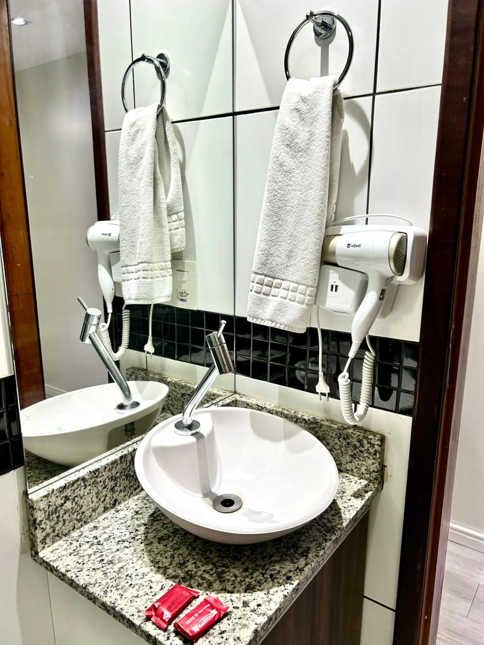 Un baño con dos lavamanos, un espejo y un secador de pelo fijado a la pared.