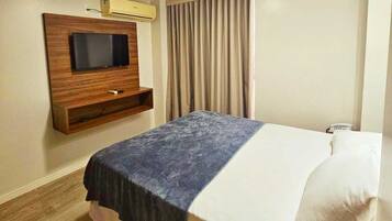 Una habitación de hotel con una cama, un televisor de pantalla plana montado en la pared, una ventana con cortinas y suelo de madera.