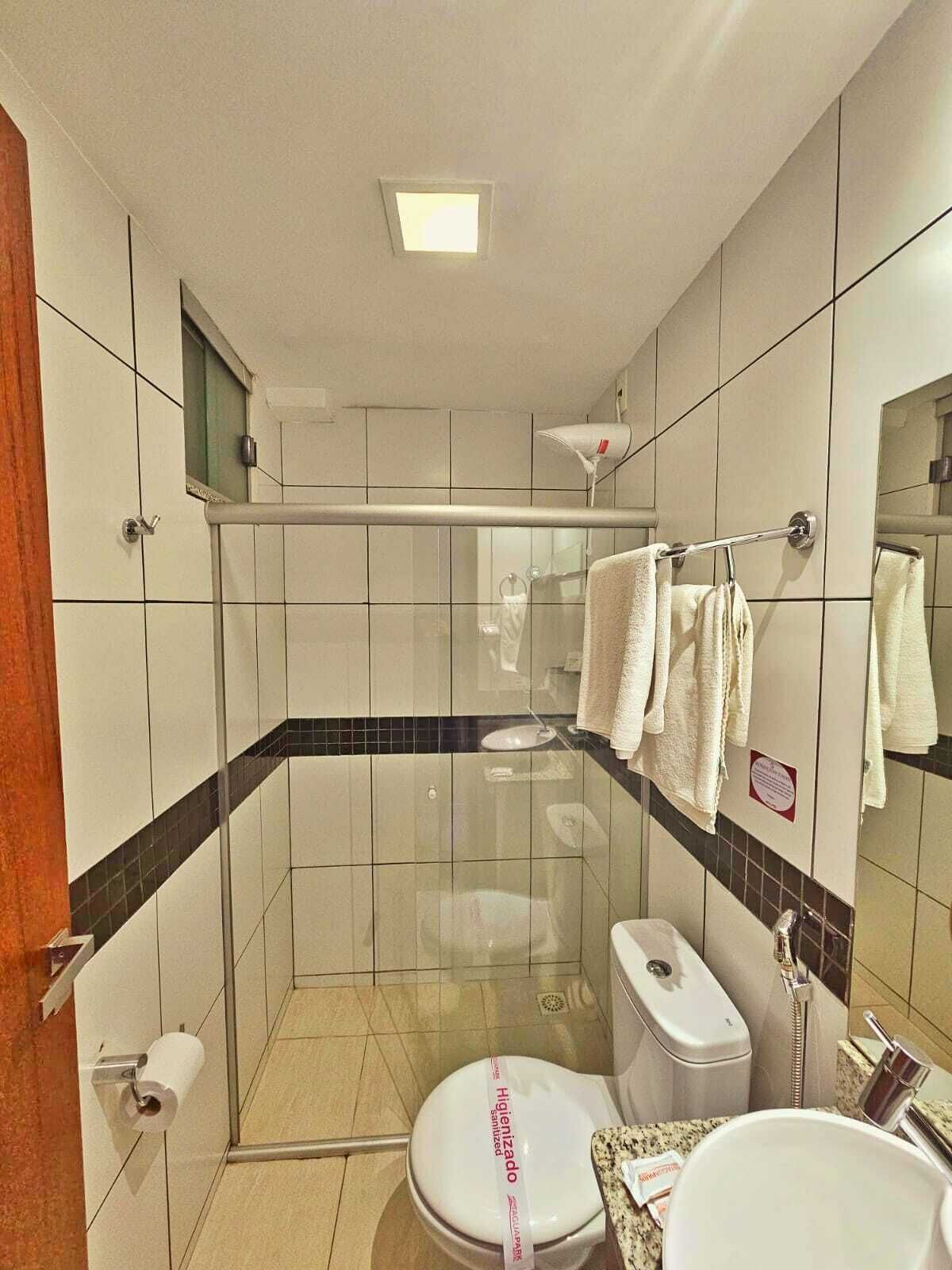 A bathroom with a glass-enclosed shower, a toilet with a 'Higienizado' label, a sink, and a mirror.