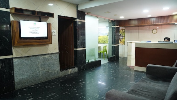 A reception area with a marble floor, a reception desk, a TV screen, and a green chair. - Olive Green Hotel (Kanayannur)