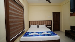 A neatly made bed with a blue checkered bedspread, a wooden headboard, and a window with horizontal blinds. - Olive Green Hotel (Kanayannur)