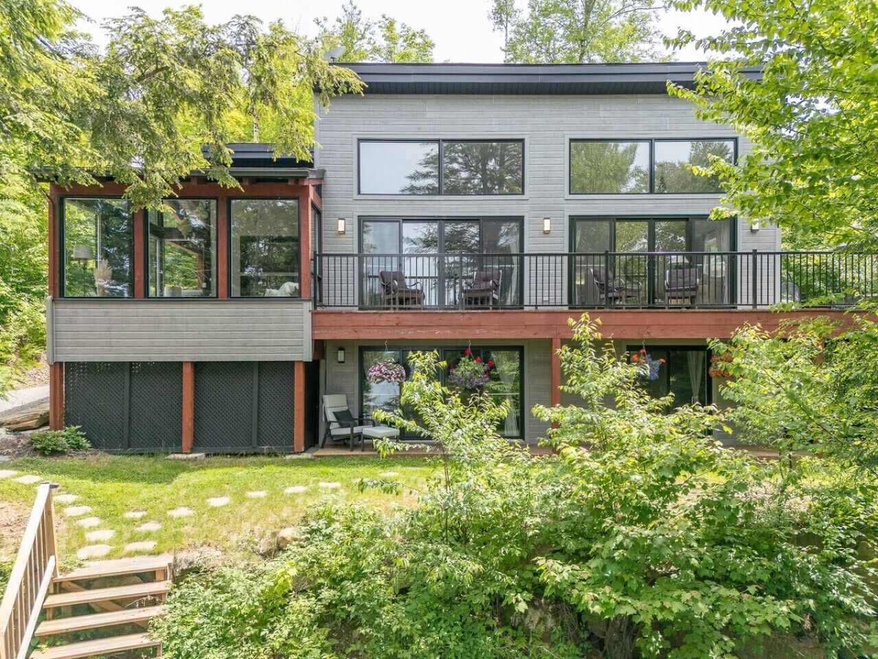 Een modern huis met twee verdiepingen, grote ramen, een balkon en een tuin.