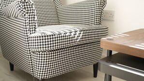 A houndstooth-patterned armchair with a wooden table beside it. - Concept Rooms  (Enfield)