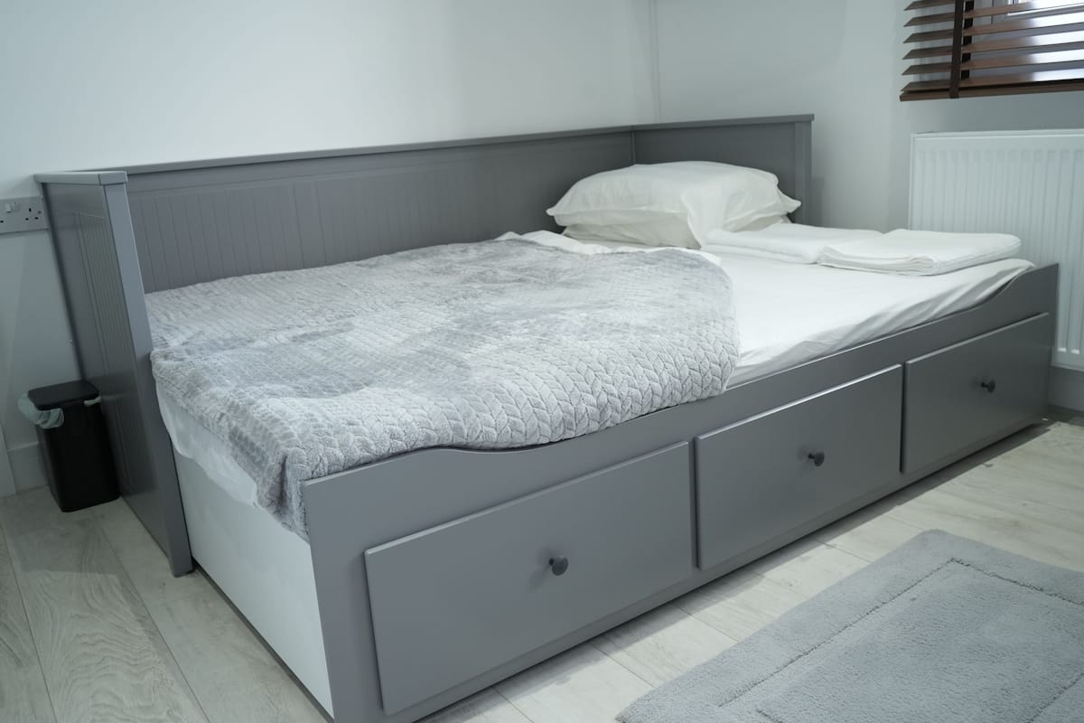 A single bed with a grey headboard and drawers, a grey blanket, and a white pillow.
