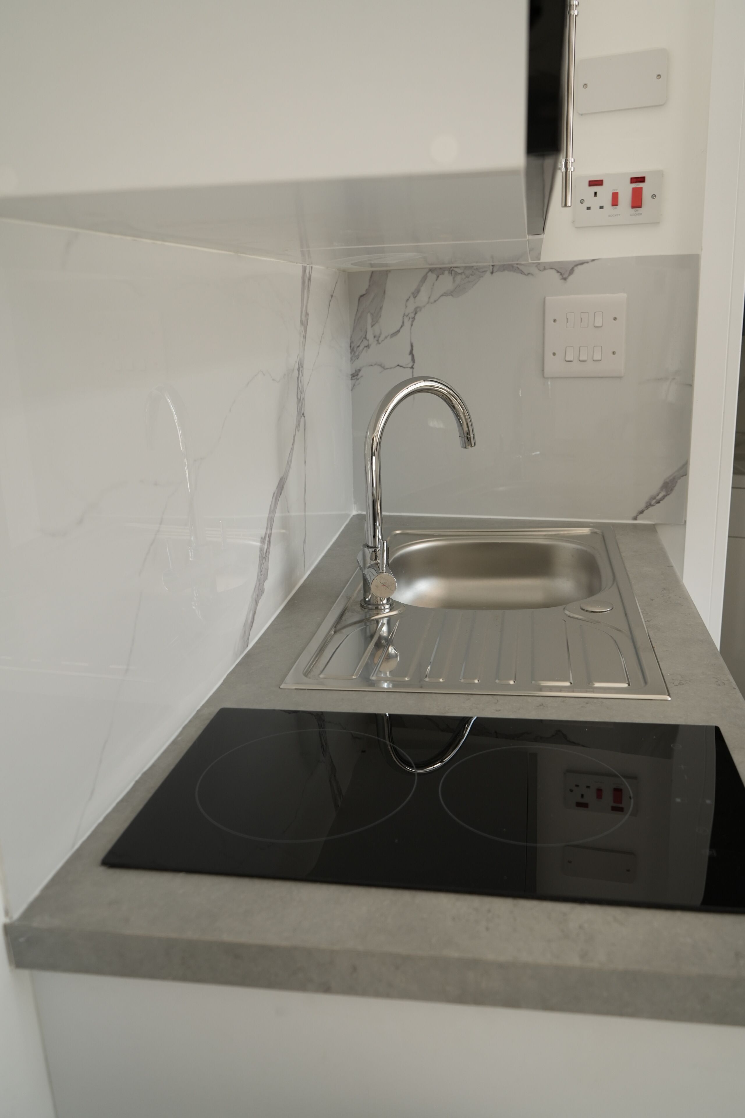 Een moderne keuken met een RVS spoelbak, een zwart inductiekookveld en een witte marmeren achterwand.
