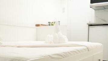 A white bedroom with a bed, a nightstand, and a microwave above a white cabinet.