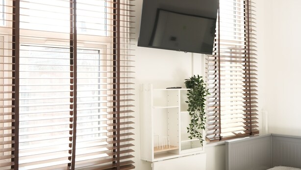 A bedroom with a bed, a TV mounted on the wall, a plant, and a desk with a chair. - Concept Rooms  (Enfield)