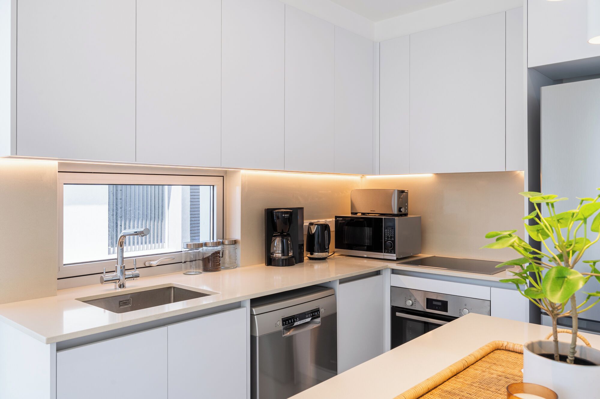 A modern kitchen with white cabinetry, a built-in microwave, a coffee maker, and a dishwasher.