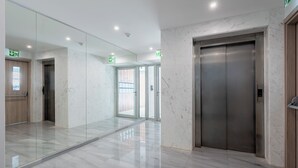 Un elevador moderno con pantalla digital, puerta de vidrio y piso de mármol.