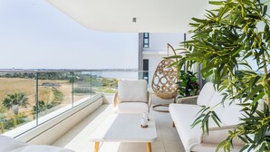 Un balcón con vistas al mar, una silla colgante, un sofá y una mesa con tazas.