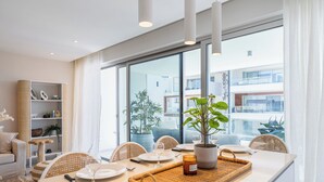 Un comedor moderno con una mesa larga, sillas de mimbre y un ventanal con vistas a edificios.