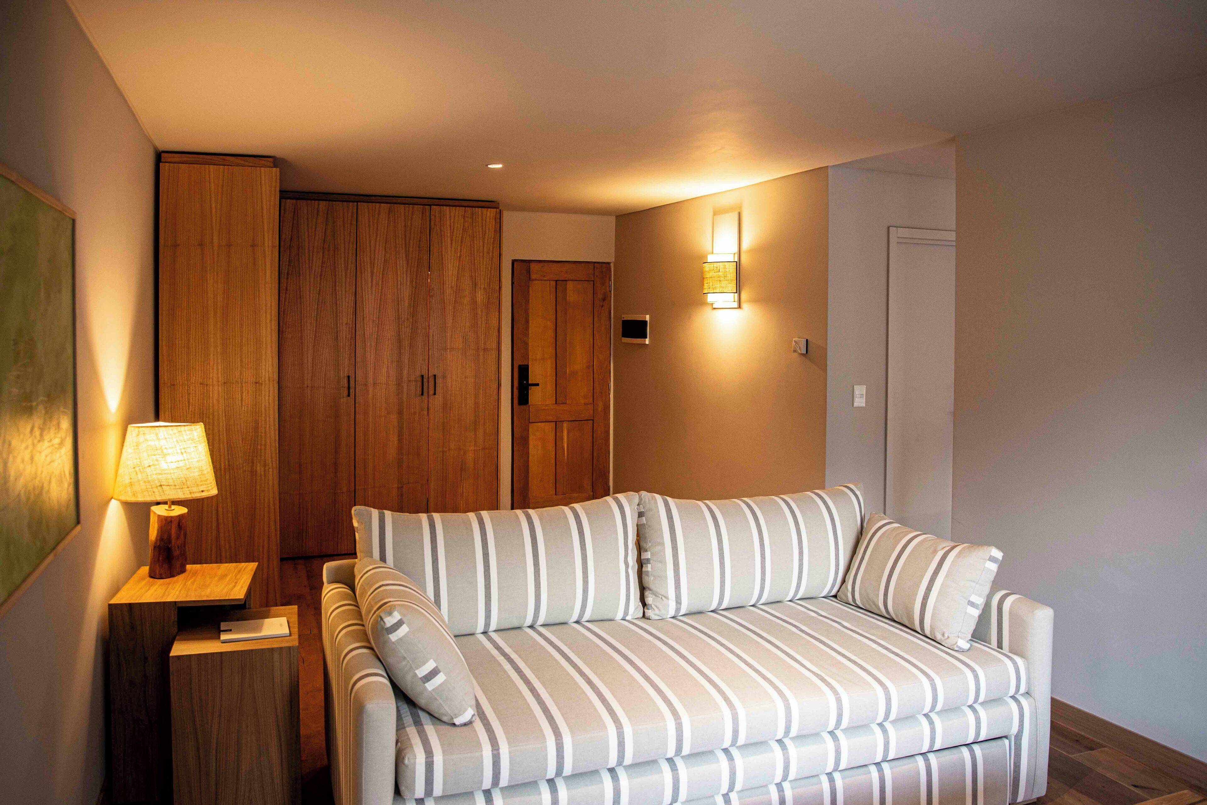 A modern living room with a striped sofa, a wooden wardrobe, and a wall-mounted lamp.
