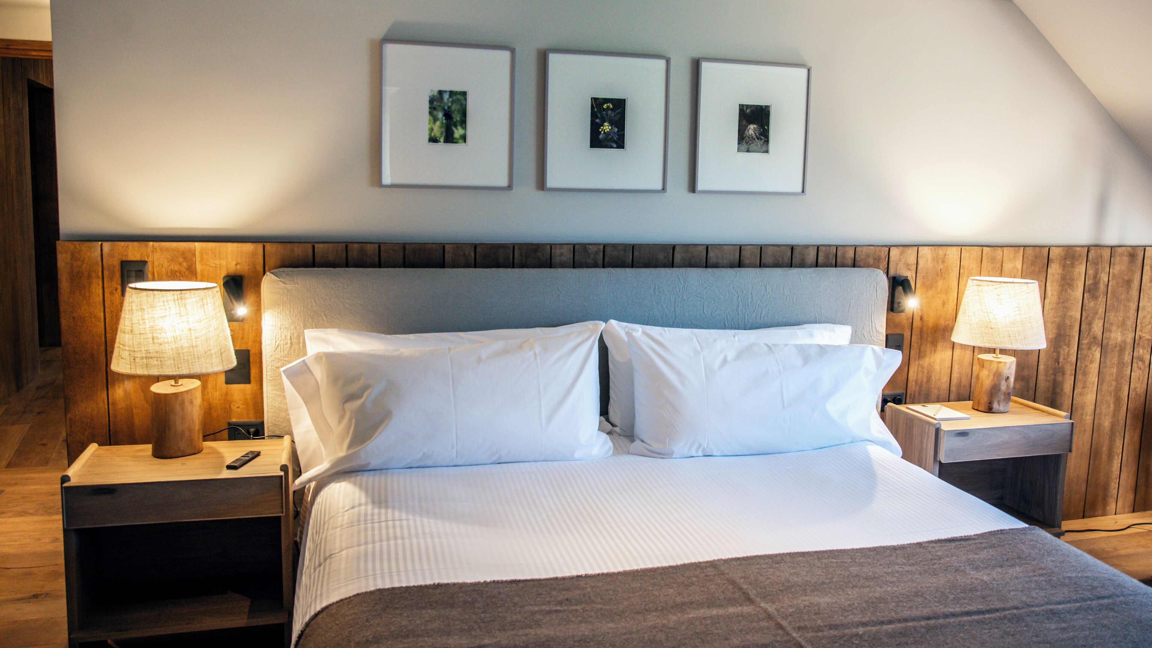 A neatly made bed with white linens, two bedside tables with lamps, and three framed pictures on the wall above the bed.