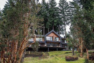 Una cabaña de troncos moderna con varios niveles y ventanas amplias, rodeada de un bosque denso.