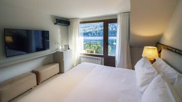 A hotel room with a bed, a TV, a desk with a chair, a window with a view of a lake, and a lamp.