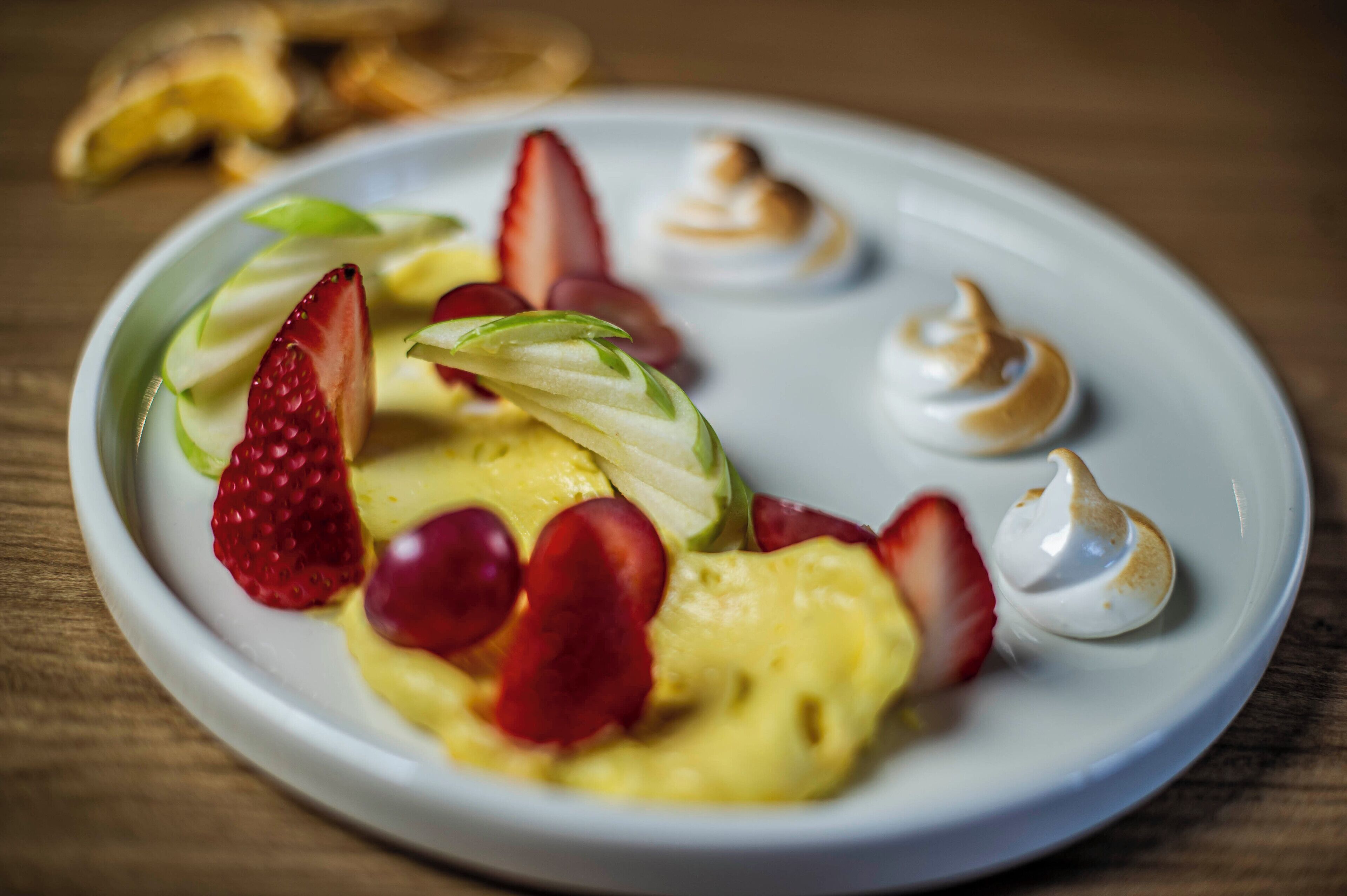 Un plato de postre con fresas, uvas y un merengue sobre una vajilla blanca.