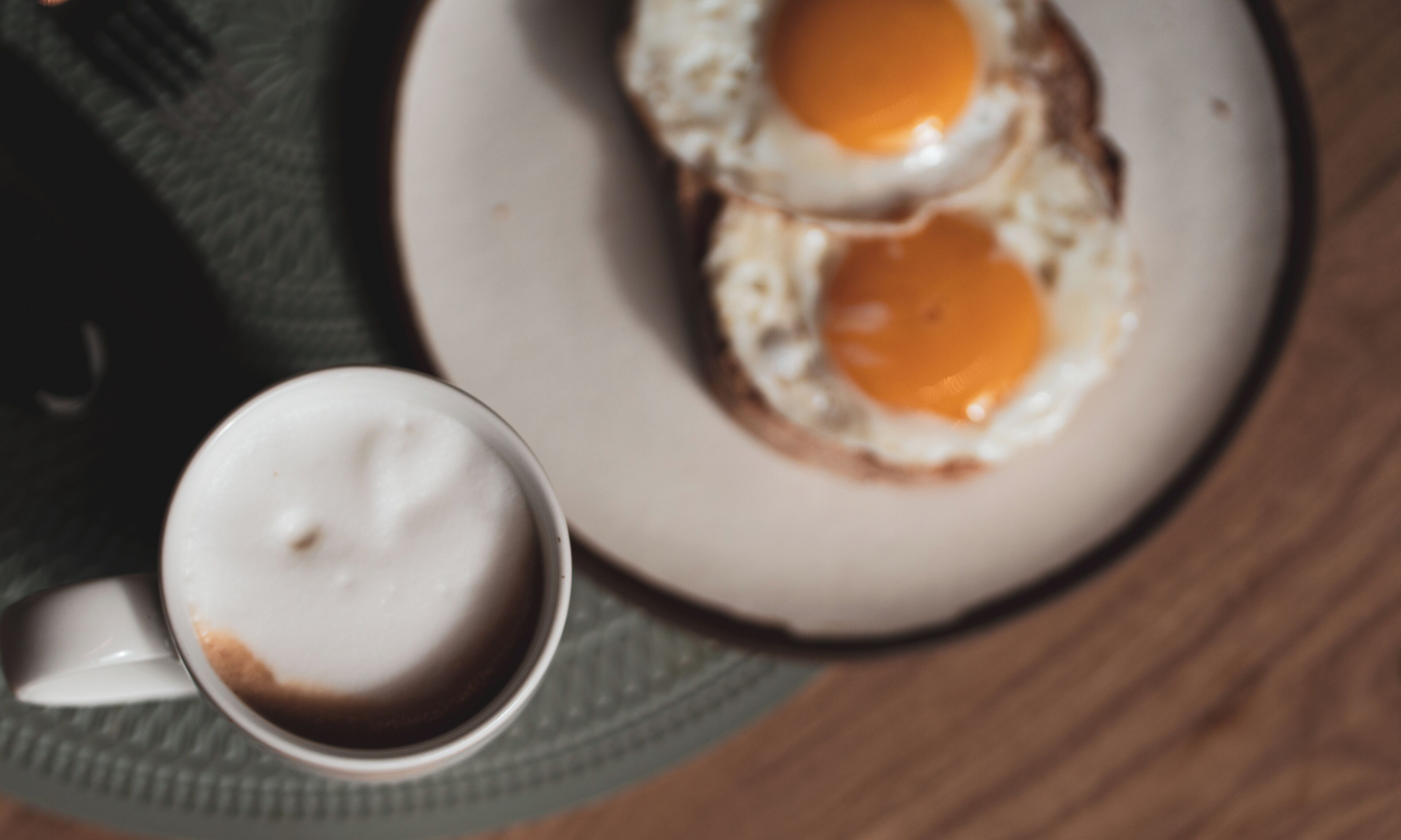 Un plato con dos huevos fritos y una taza de café sobre una mesa.