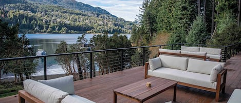 Une terrasse dotée de mobilier d’extérieur, offrant une vue sur un lac et des collines boisées.