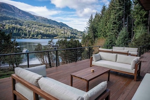 Una terraza con mobiliario exterior con vistas a un lago y colinas boscosas.