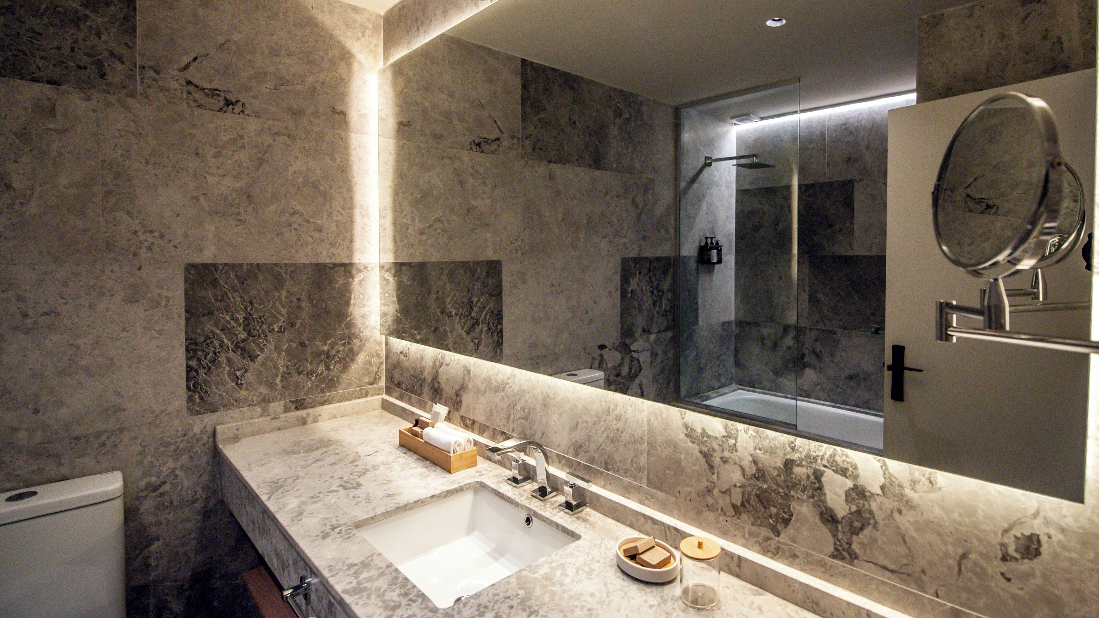 Un baño moderno con lavamanos de mármol, un espejo grande y cabina de ducha con paredes de vidrio.
