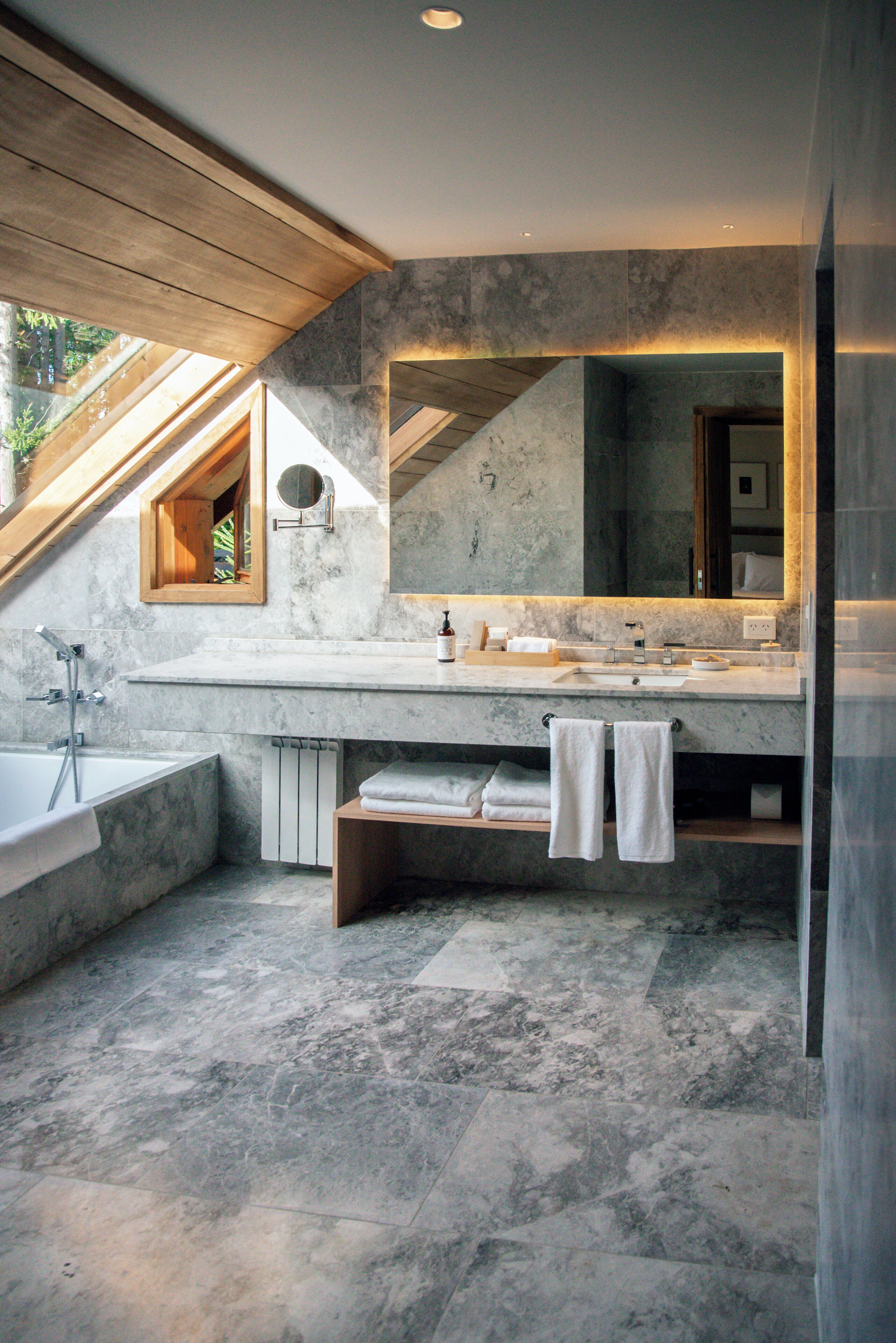 A modern bathroom with a skylight, a large mirror, a bathtub, and a vanity with a sink and towel rack.