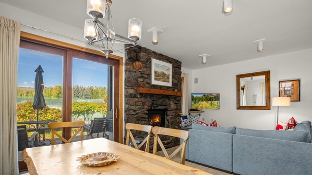 A dining area with a wooden table and chairs, a stone fireplace, and a view of the outdoors.
