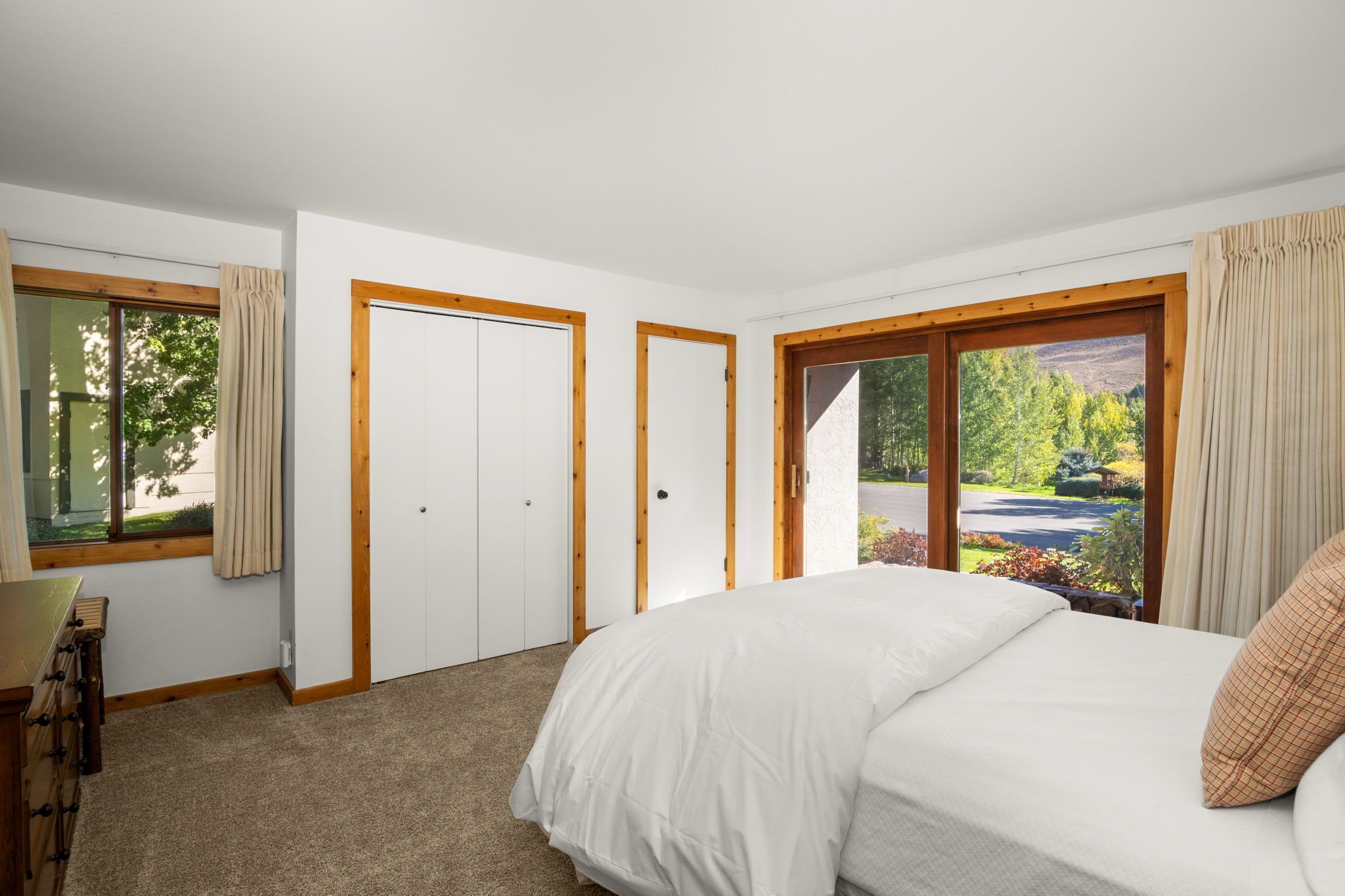 Quarto com uma cama grande, uma escrivaninha e vista para uma paisagem verde através de uma porta de vidro deslizante.