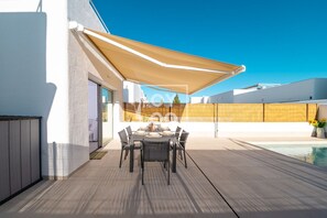Un patio con tavolo e sedie, una piscina e una zona coperta con vista sui dintorni.