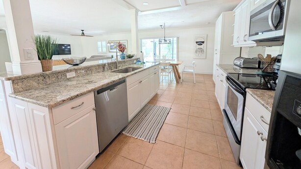 A modern kitchen with white cabinetry, granite countertops, a dishwasher, a microwave, and a stove.