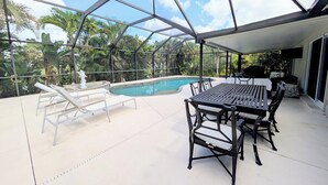 A covered outdoor area with a pool, lounge chairs, and a dining table.