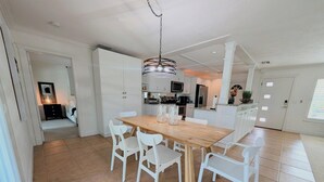 A modern kitchen with white cabinetry, a wooden dining table, and white chairs.